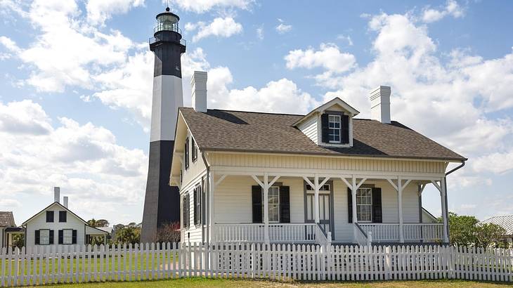 A black and white striped lighthouse next to small white houses and green grass