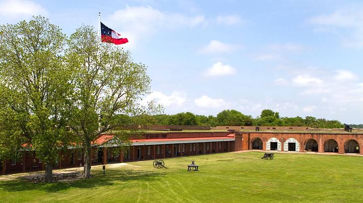 Green grass, trees, and a flag next to the walls of a historic fort