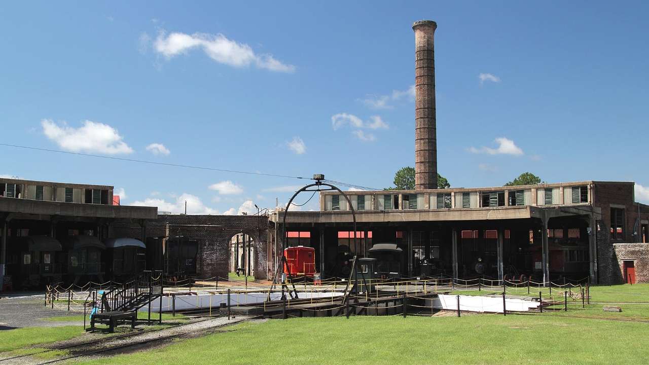 A stone building with a large chimney tower and a red train car next to the grass