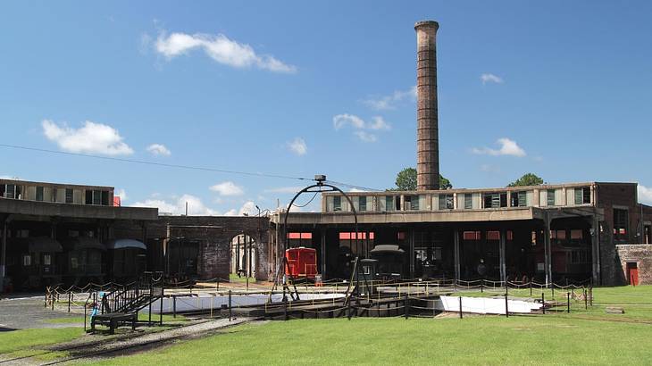 A stone building with a large chimney tower and a red train car next to the grass