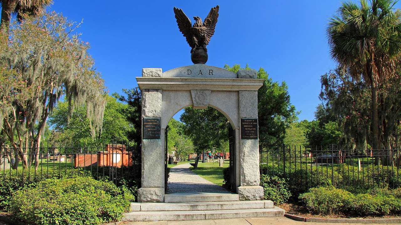 A stone arch with an eagle statue on top surrounded by greenery under a blue sky
