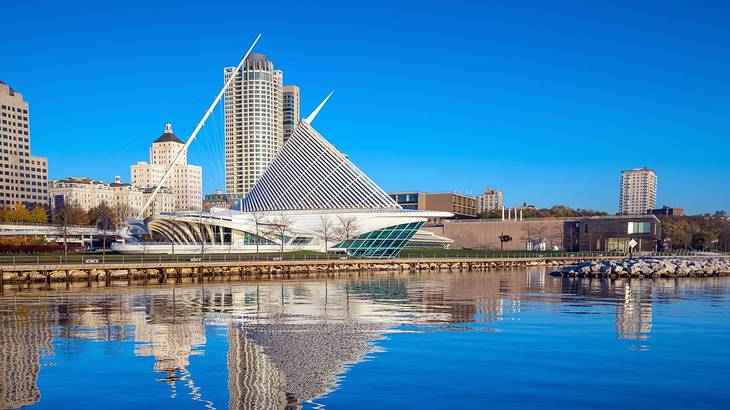 A city skyline with buildings and a modern structure next to a river on a clear day