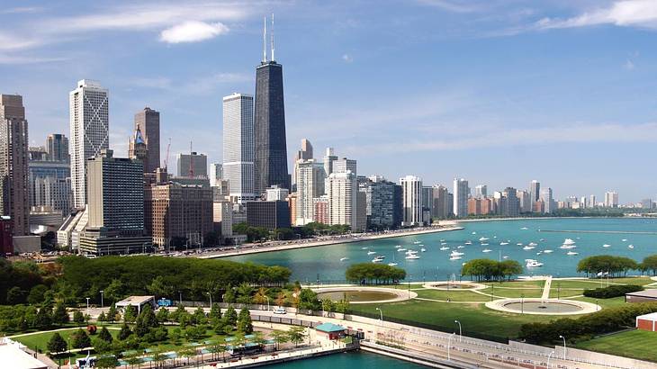 The Chicago city skyline next to a river and green park under a blue sky with clouds