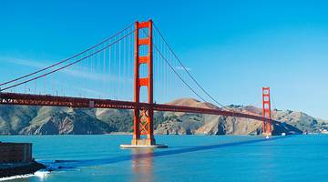 The Golden Gate Bridge over water with hills on one side under a clear blue sky