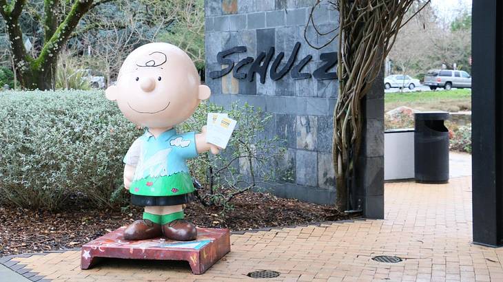 A Charlie Brown statue next to a wall with a sign that says "Schulz"