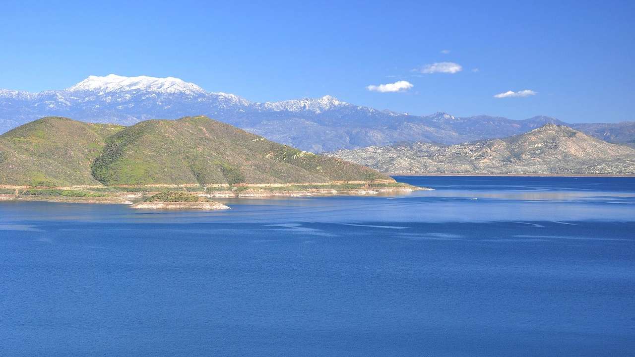 A lake with greenery-covered hills and snow-capped mountains around it