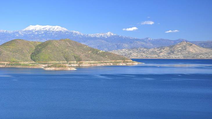 A lake with greenery-covered hills and snow-capped mountains around it