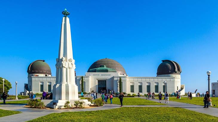 A white building with three domes next to grass and a white statue