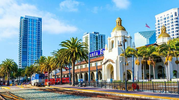 A railway track next to palm trees and a white stone building with a gold dome