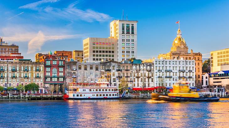 Water with old-fashioned boats on it next to small city buildings under a blue sky