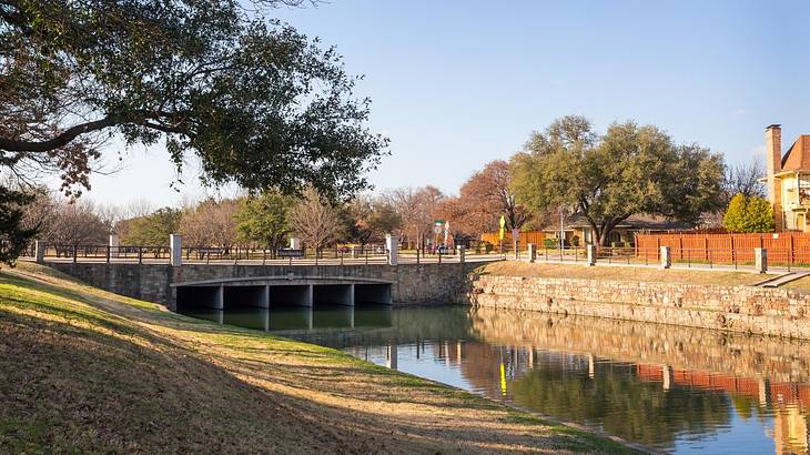 A river with a bridge over it next to a grassy hill and trees