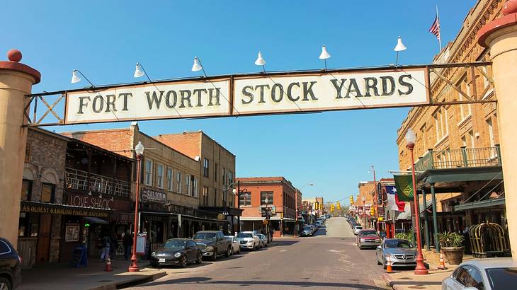 An old-fashioned sign over a street that says "Fort Worth Stock Yards"