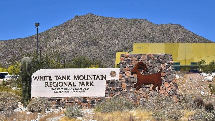 A mountain, shrubs, and a cactus next to a "White Tank Mountain Regional Park" sign