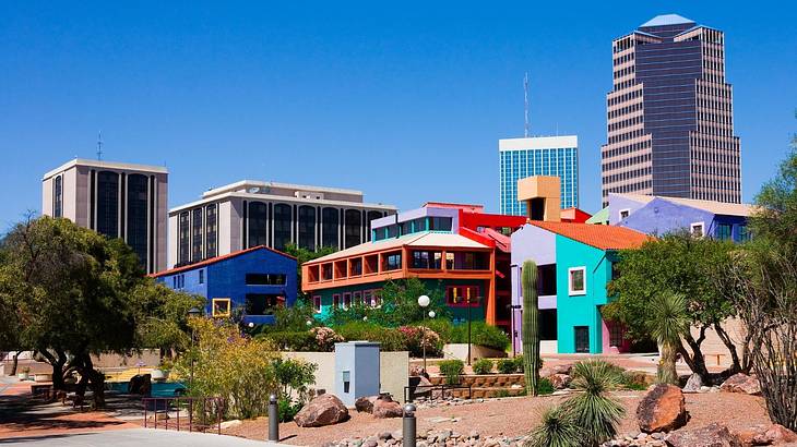 Brightly colored houses next to trees with tall city buildings behind them
