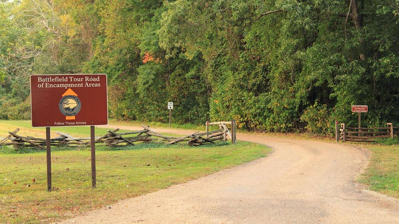A dirt road through grass and trees next to a sign that says "Battlefield Tour Road"