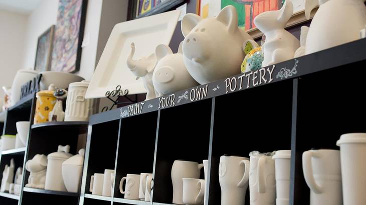 A shelf with unpainted pottery pieces and the words "Paint Your Own Pottery"