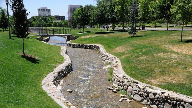 A small stream with grass on either side and city buildings in the distance A small stream with grass on either side and city buildings in the distance