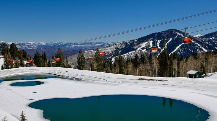 A snow-covered mountain with a small pool of water and a ski lift next to it