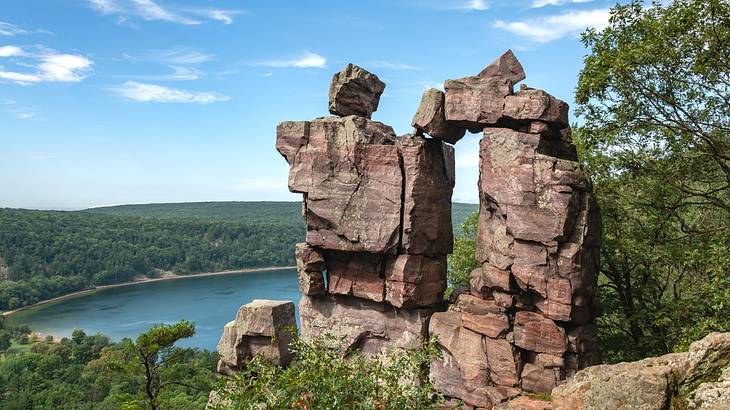 A rock formation surrounded by greenery sitting above a lake and a forest A rock formation surrounded by greenery sitting above a lake and a forest