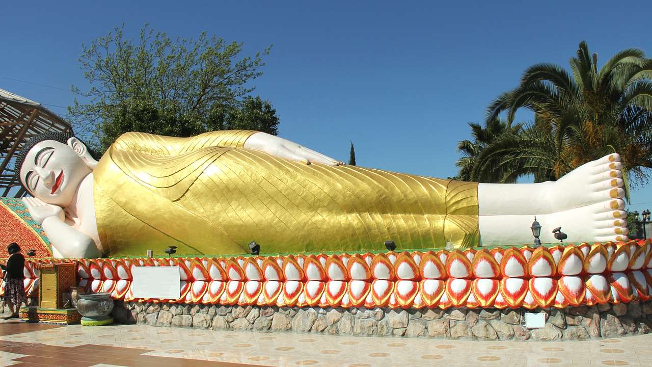 A statue of a reclining Buddha with trees behind it under a blue sky