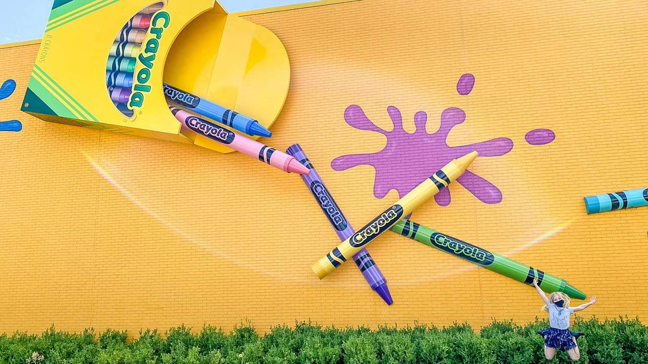 A yellow wall with a large Crayola box attached and crayons falling out of it
