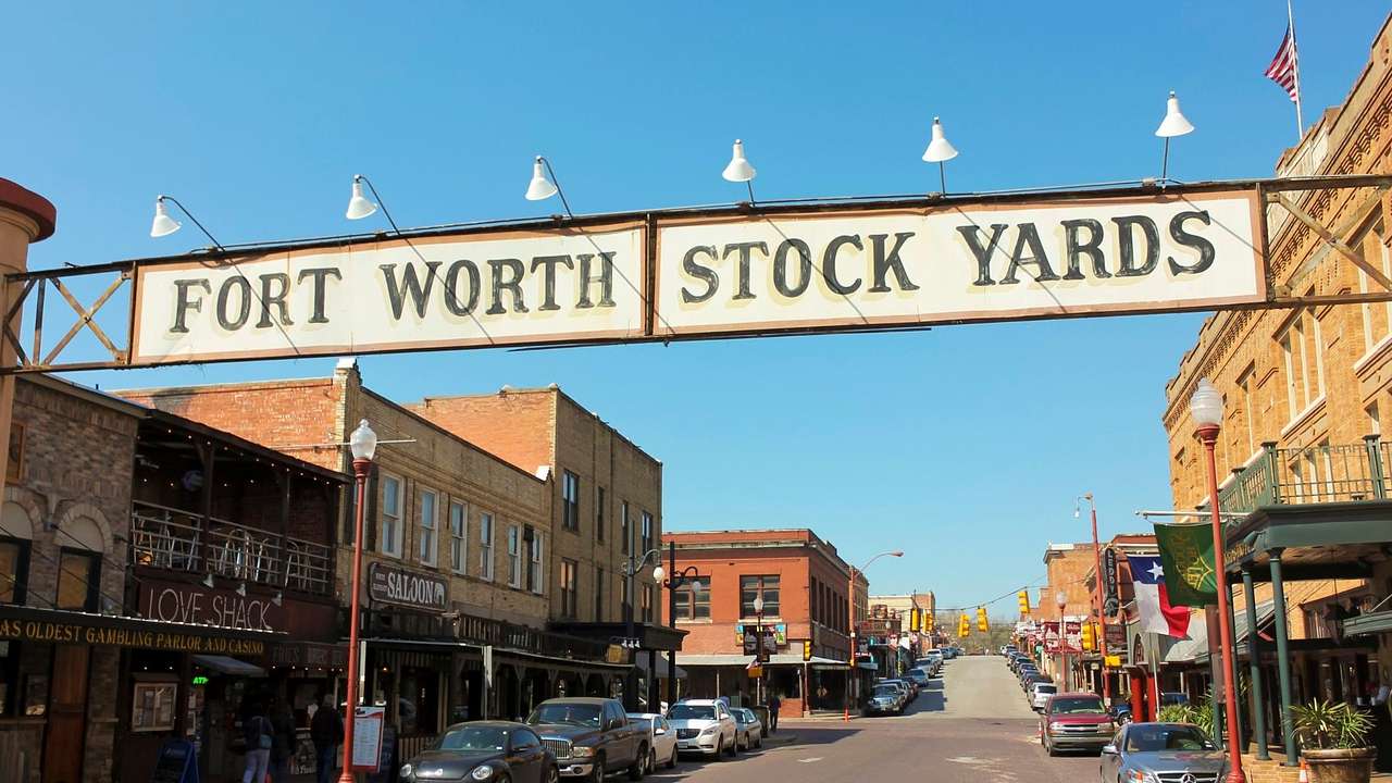 A sign that says "Fort Worth Stock Yards" over a street with old-fashioned buildings
