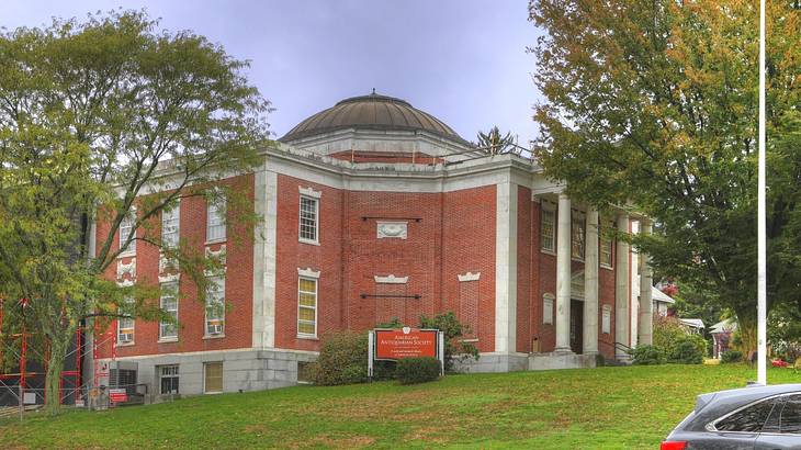 A red brick building with white details and a domed roof next to grass and trees