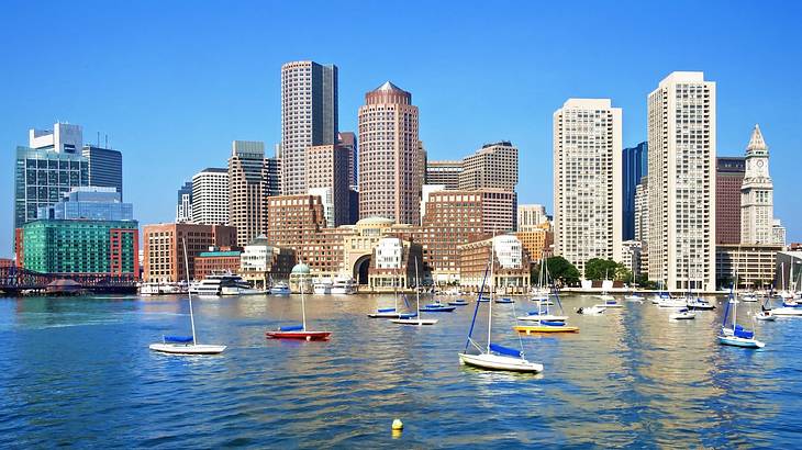 Small boats on a lake next to a city skyline under a clear blue sky