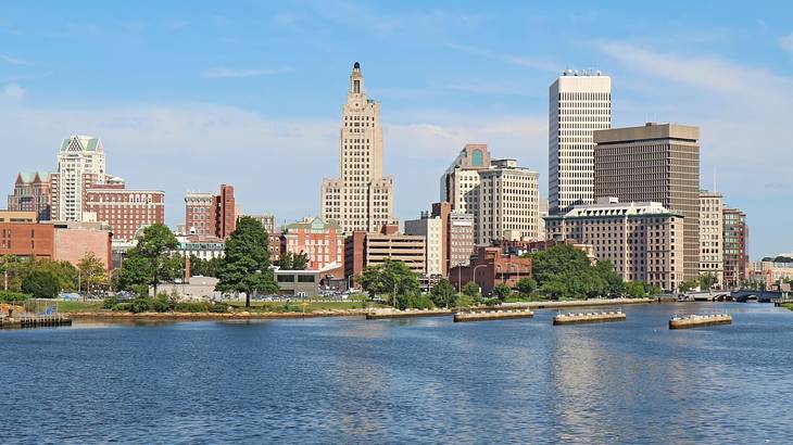 A city skyline with trees and buildings next to the water under a blue sky