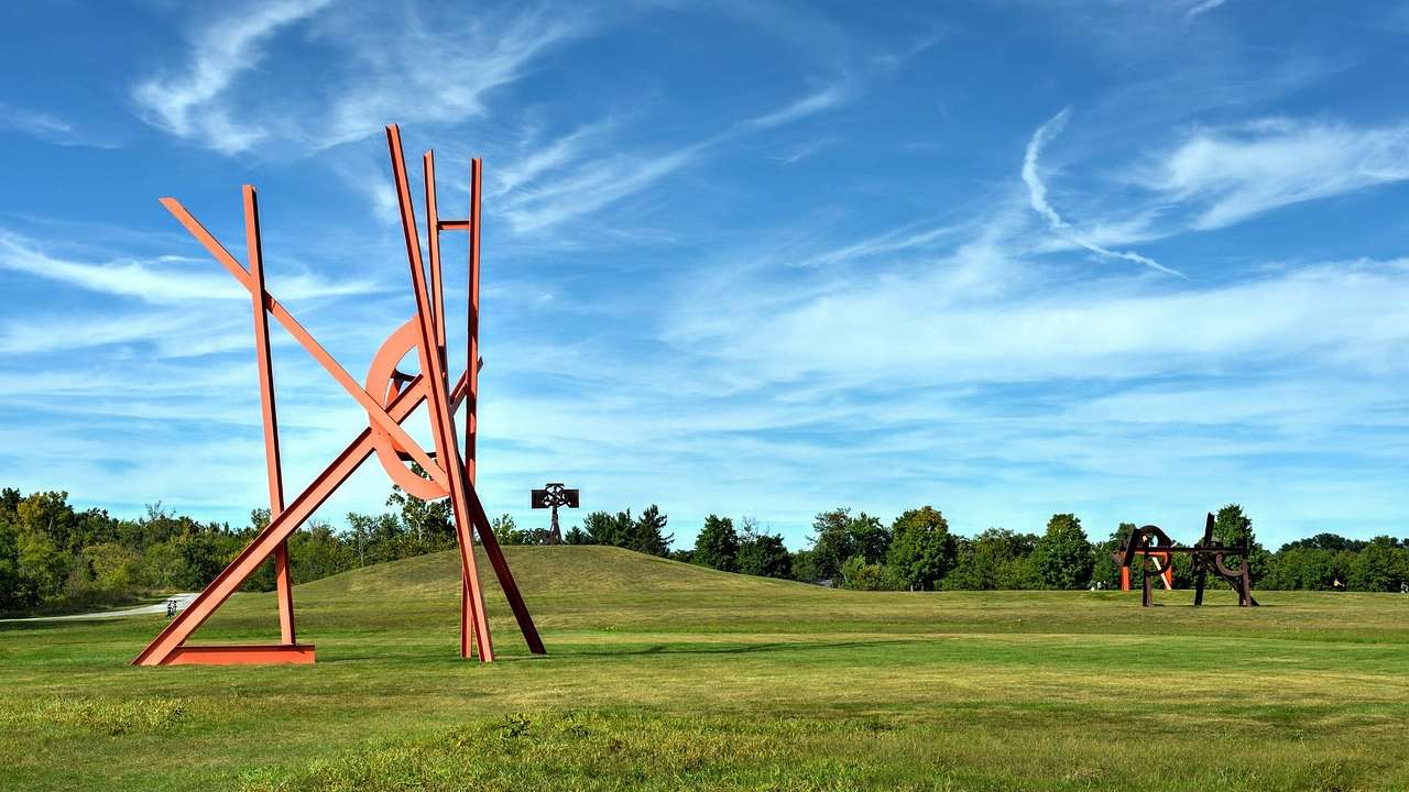A red contemporary art sculpture on the grass under a blue sky with some cloud
