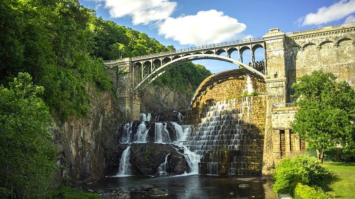 A bridge over a dam with a small waterfall and green trees around it