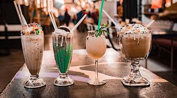 Four milkshakes on a table in different shaped glasses and with various toppings