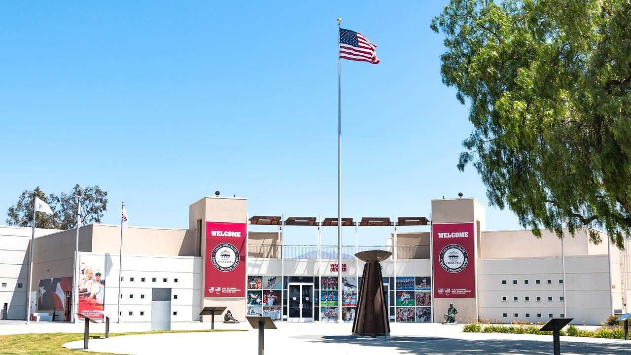 A modern building with red banners and a sculpture, trees, and a US flag in front