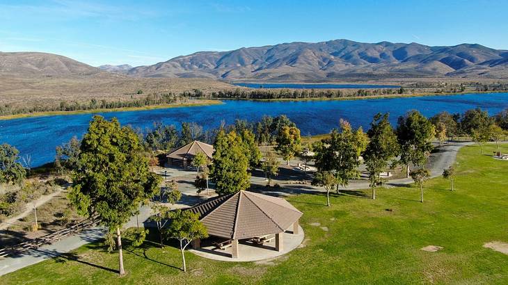 A view of a park with trees next to a lake and hills