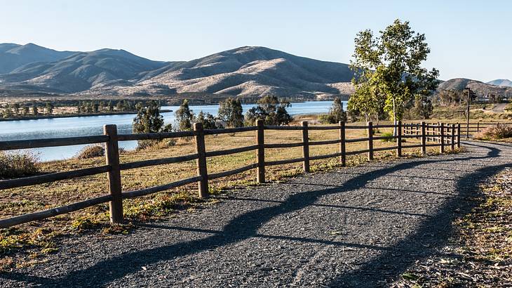 A dirt path next to a fence, grass, a reservoir, and hills