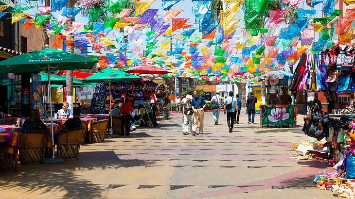 A street with patio tables and umbrellas and colorful flags across it