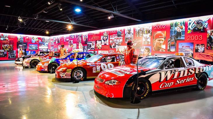 Red NASCAR cars in an exhibit with a wall of photos behind them