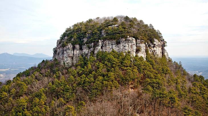 A rock mountain covered in greenery under a hazy sky