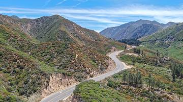 Greenery-covered mountains with a road winding through them under a blue sky