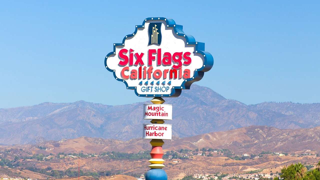 A sign that says "Six Flags California" with mountains behind it