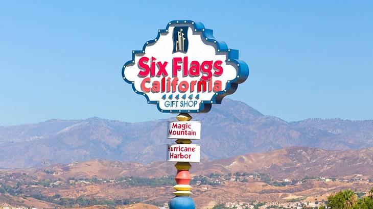 A sign that says "Six Flags California" with mountains behind it