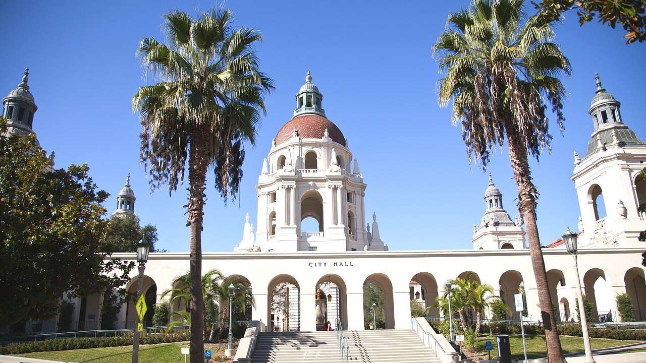A white stone building with a dome roof and arches surrounded by palm trees