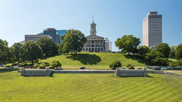 A grassy area with trees and a state capitol building in the distance on a clear day