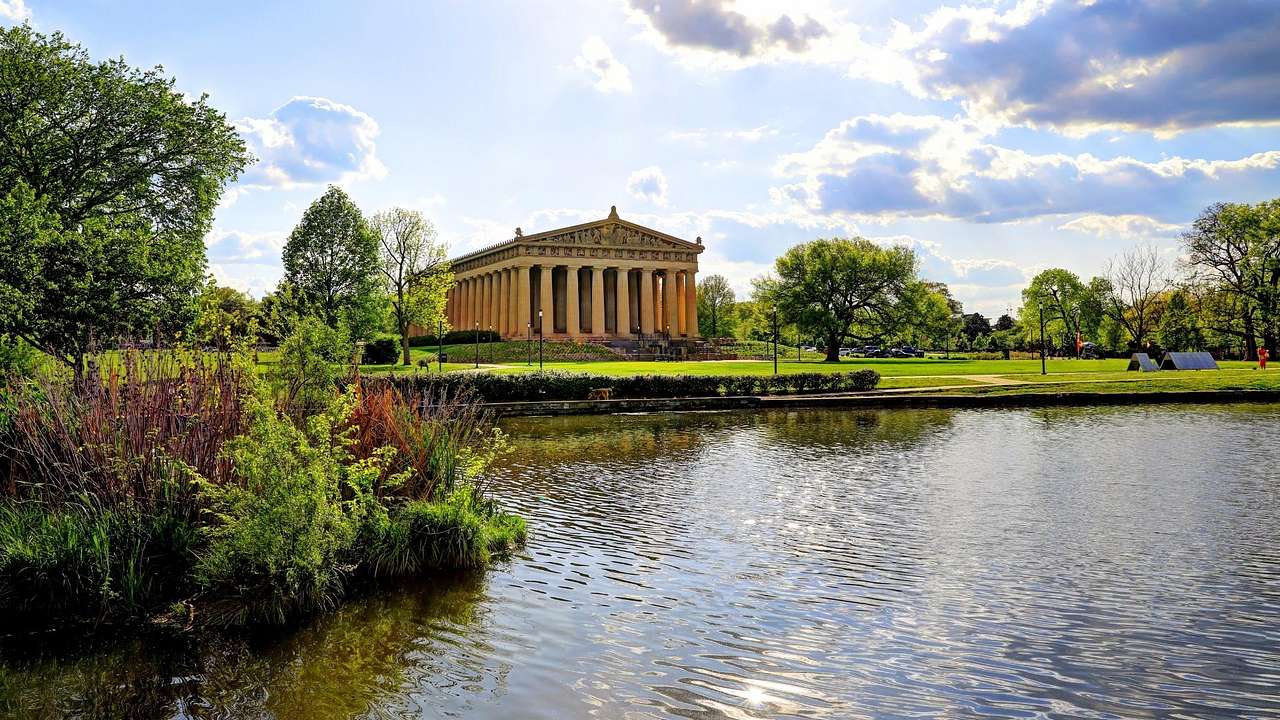A lake with greenery around it and a Parthenon structure on the grass next to it