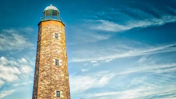 A brick lighthouse in front of a blue sky with some cloud
