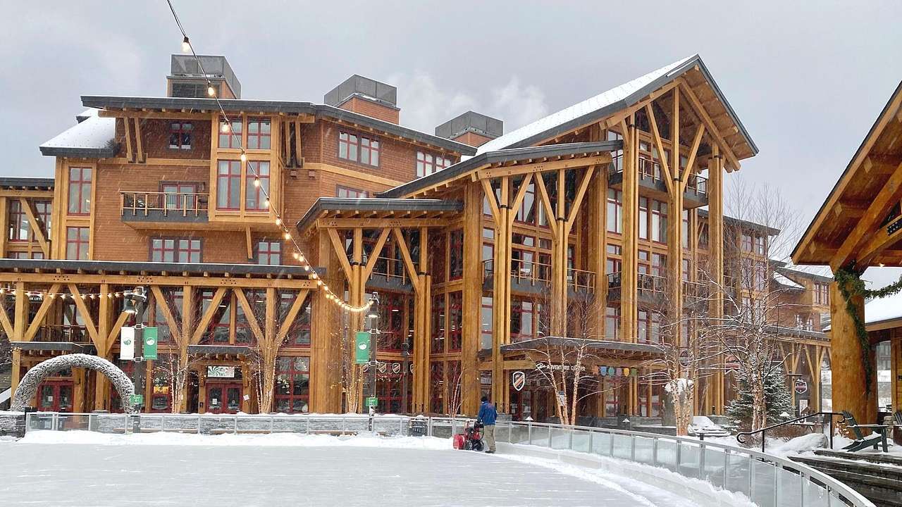 A wooden ski resort lodge with an ice rink in front of it under a snowy sky