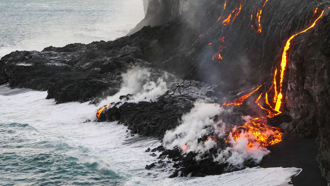 Lava flowing down a cliff into the ocean creating steam once it meets the ocean