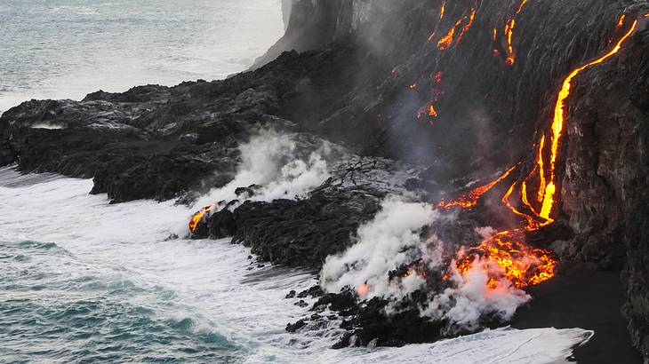 Lava flowing down a cliff into the ocean creating steam once it meets the ocean
