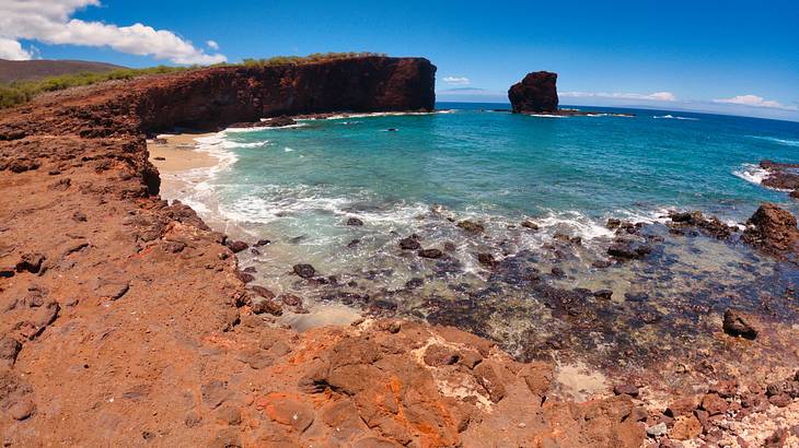 A brown rocky shoreline with turquoise water and clear blue skies