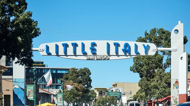 A sign over a street that says "Little Italy, San Diego" next to trees and buildings